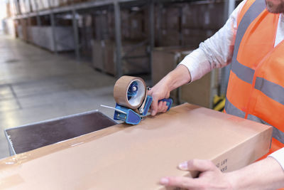 Man in factory hall wearing safety vest closing cardboard boax