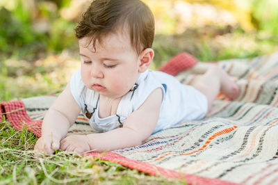 Cute baby boy lying on picnic blanket over grass