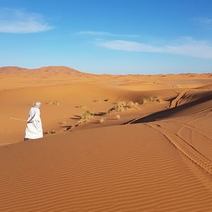 Rear view of man walking at desert against sky