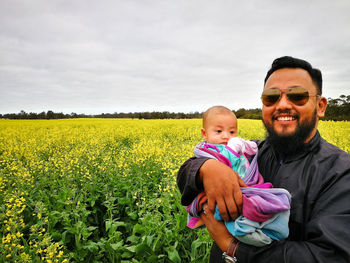 Portrait of father carrying daughter on field against sky