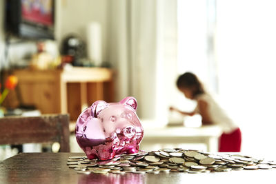 Close-up of coins and piggy bank on table with girl in background