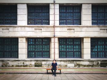 Man sitting on bench against building