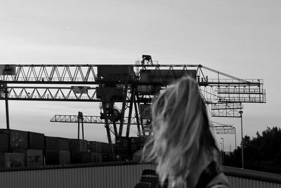Rear view of woman walking at harbor against cranes