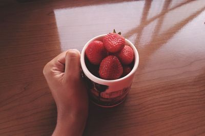 Cropped hand holding strawberries in cup on table