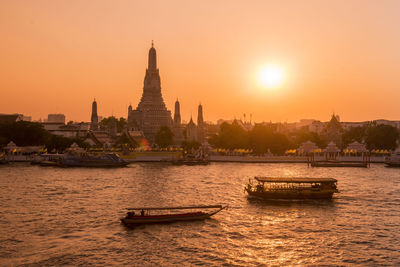 Boat in river by buildings against sky during sunset