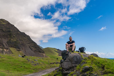 Man sitting on rock by mountain against sky