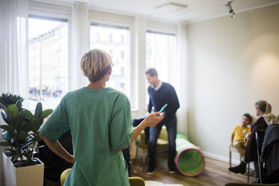 Rear view of pediatrician with pen calling out names while standing in hospital