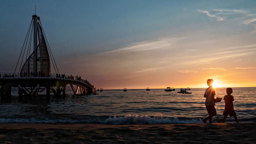 People at beach against sky during sunset