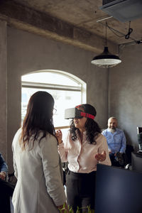 Businesswoman wearing vr simulator while gesturing by female colleague at office