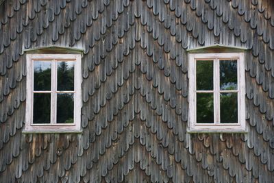 2 windows in a house gable with wooden shingles.