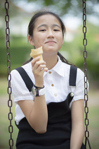 Portrait of smiling girl eating ice cream while sitting on swing