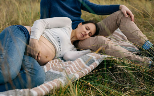 Pregnant woman relaxing with man on field