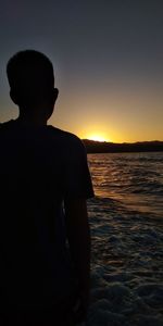 Rear view of silhouette man standing by sea against sky during sunset