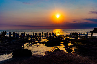 Silhouette people on beach against sky during sunset