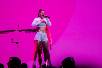 Full length portrait of woman standing against pink wall