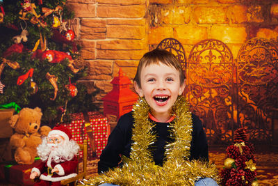 Smiling boy sitting next to a christmas tree  wrapped in shiny christmas decoration. merry christmas