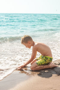 Shirtless boy playing on shore at beach during summer