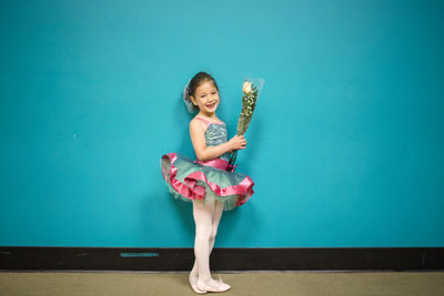 A little girl stands in a dance costume holding a bunch of flowers