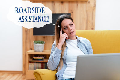 Young woman using smart phone while sitting on laptop