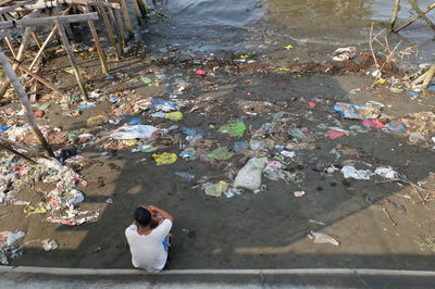 Rear view of man sitting by washed up garbage