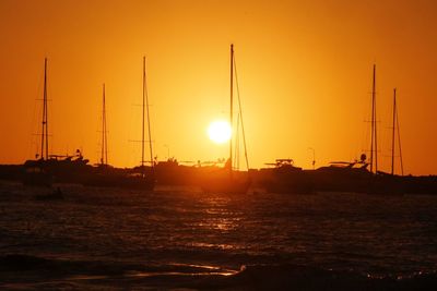 Silhouette sailboats in sea against orange sky