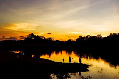 Silhouette trees by lake against sky during sunset