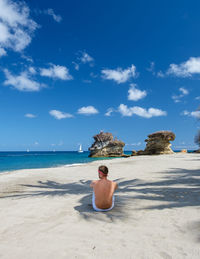 Rear view of woman sitting on beach against sky