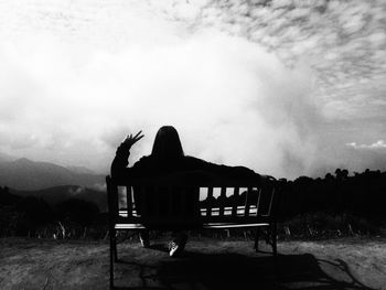 Silhouette of woman sitting on bench against sky