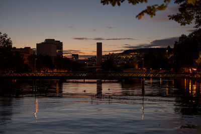 Silhouette buildings by lake against sky at sunset