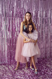 Beautiful girl with big eyes in pink dress and her mom holding garland on background christmas tree
