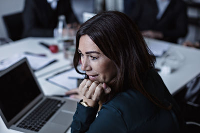 High angle view of businesswoman with hand on chin looking while sitting at conference table in board room