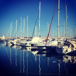 Sailboats moored in sea against clear blue sky