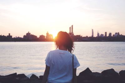 Rear view of woman standing on groyne against skyline during sunset