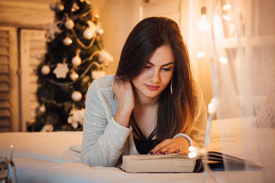 Woman reading book while lying on bed at home during christmas