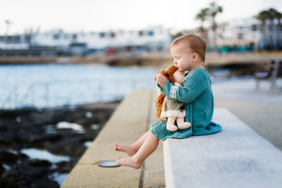 Cute girl with doll sitting on retaining wall