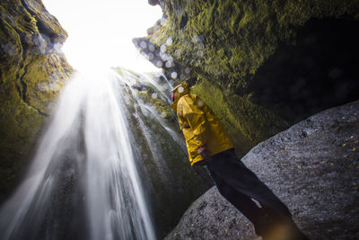 Low angle view of man wearing raincoat while looking at waterfall