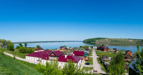 High angle view of houses by sea against clear blue sky