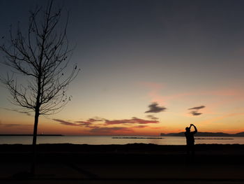 Silhouette person standing by sea against sky during sunset