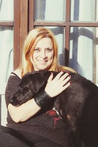 Portrait of smiling beautiful woman embracing dog while sitting on bench against house