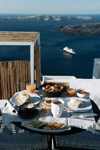Breakfast table with coffee, bun, juice, and cake on a coast house with a view of ocean and island