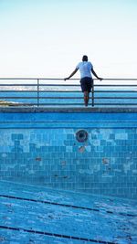Rear view of man standing by abandoned  swimming pool against sky