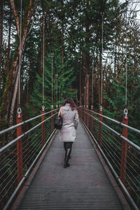 Rear view of woman walking on footbridge in forest