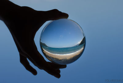 Close-up of hand holding crystal ball against clear blue sky