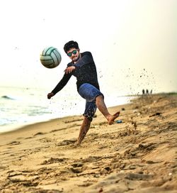 Young man playing soccer at beach against clear sky