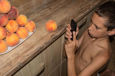 High angle view of shirtless boy photographing fruit through mobile phone