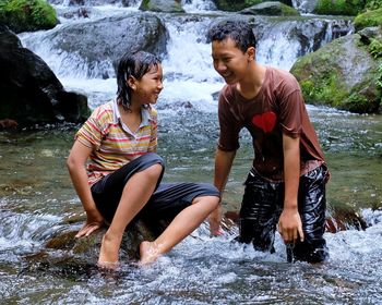 Young couple sitting on rock at waterfall