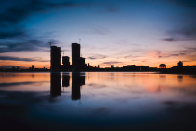 Reflection of city in lake against sky during sunset