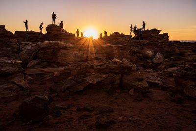 Silhouette people on rock against sky during sunset