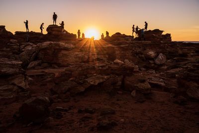 Silhouette people on rock against sky during sunset