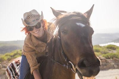 Portrait of happy young woman riding horse against clear sky during sunny day